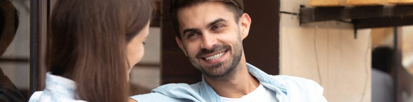 Man smiling at woman as they sit on a couch talking.