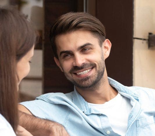 Man smiling at woman as they sit on a couch talking.