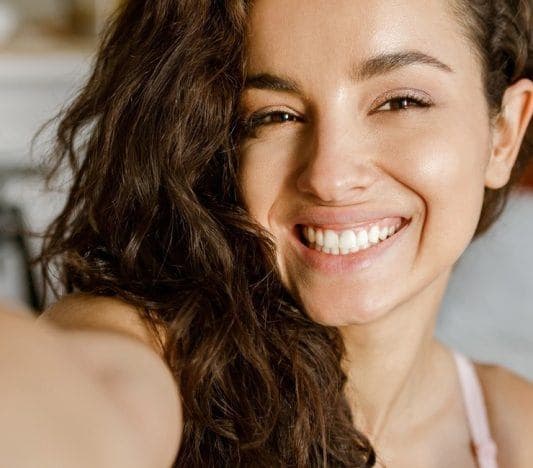 Beautiful woman with curly hair and natural makeup taking a selfie.