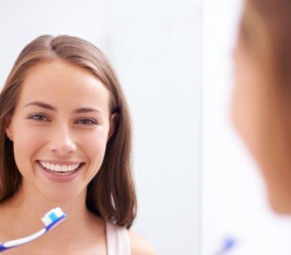 A woman holding a toothbrush and looking at the mirror.