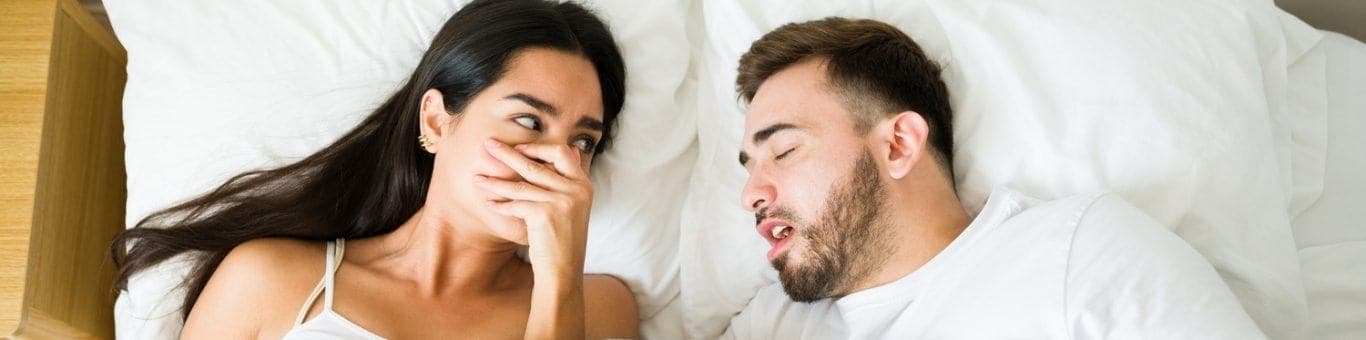 Woman covering nose in bed, bothered by partner’s bad breath.