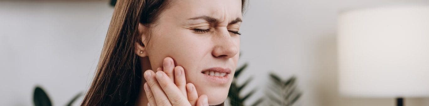 A woman looking unhappy, holding her jaw.