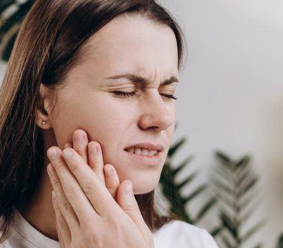 A woman looking unhappy, holding her jaw.