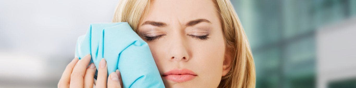 Woman with eyes closed frowning and holding an ice bag to her jaw.