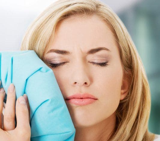 Woman with eyes closed frowning and holding an ice bag to her jaw.