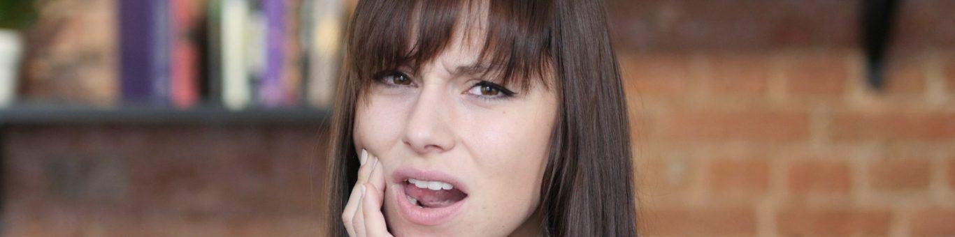 Caucasian woman with brown hair holding her cheek with tooth pain.