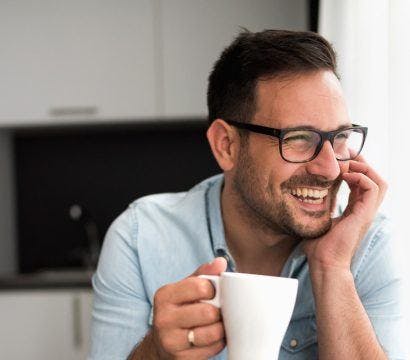 Man in glasses drinking mug on the counter while laughing.