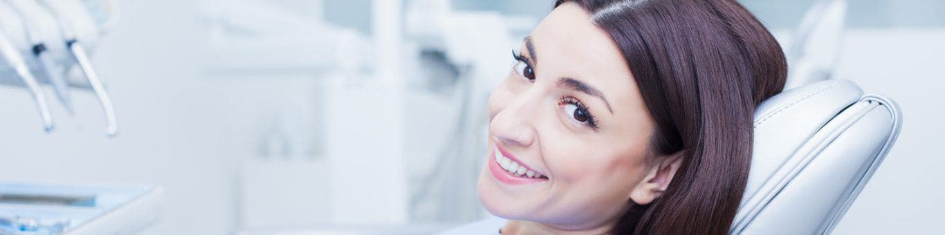 Smiling woman in a dental chair making okay ring gesture with one hand.