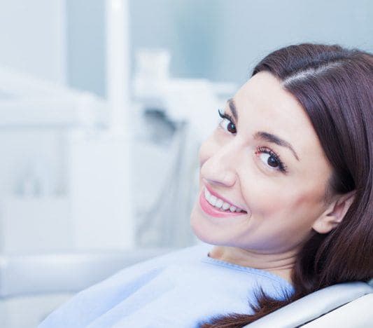 Smiling woman in a dental chair making okay ring gesture with one hand.