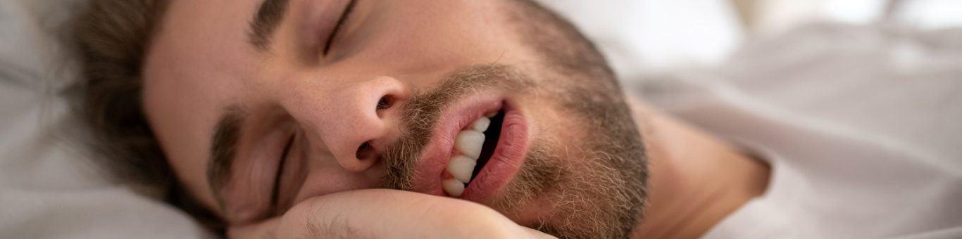 Man sleeping with mouth open on white bed.