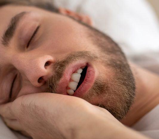 Man sleeping with mouth open on white bed.