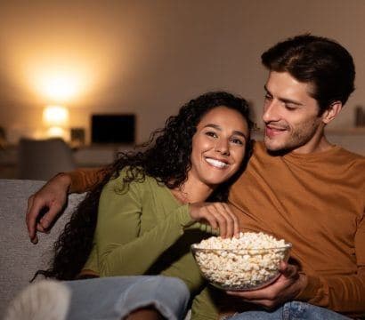 Young couple cuddled up on couch watching movie and eating popcorn.