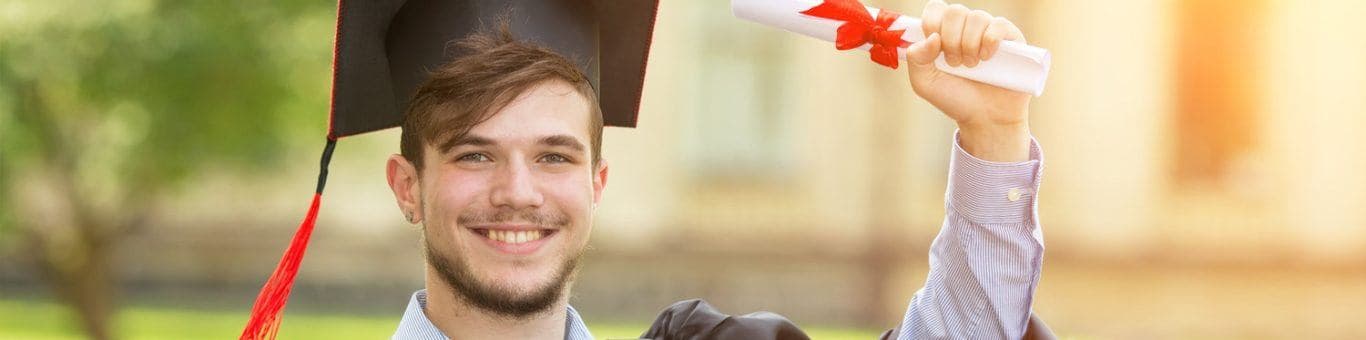 Young man with beard wearing toga and mortarboard and holding a diploma.