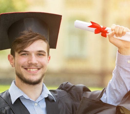 Young man with beard wearing toga and mortarboard and holding a diploma.