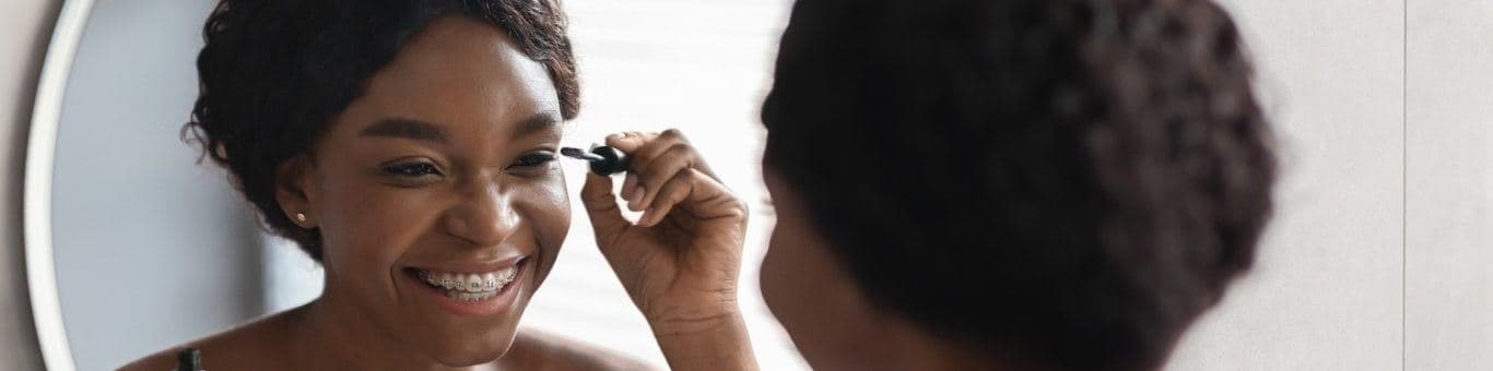 Beautiful black woman applying mascara in front of mirror.