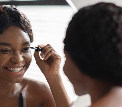 Beautiful black woman applying mascara in front of mirror.