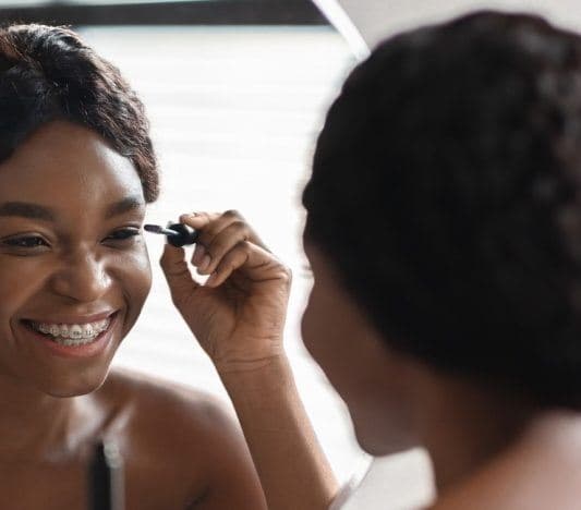 Beautiful black woman applying mascara in front of mirror.