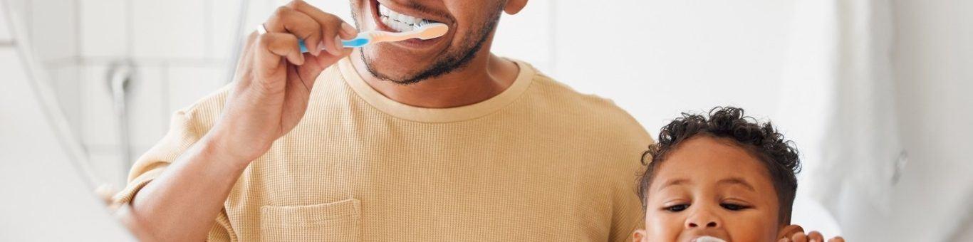 Father and son brushing teeth in front of mirror.