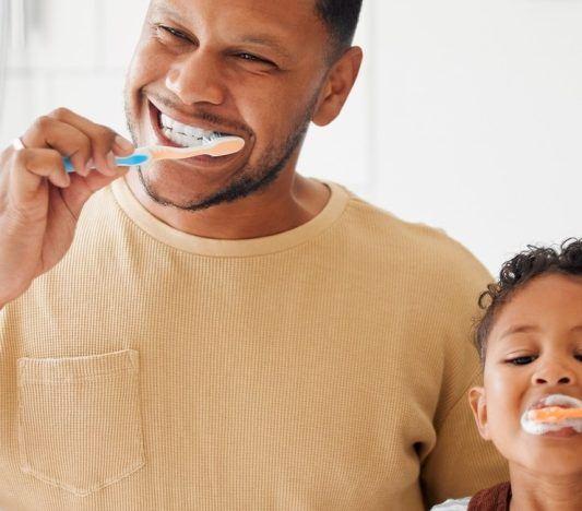 Father and son brushing teeth in front of mirror.