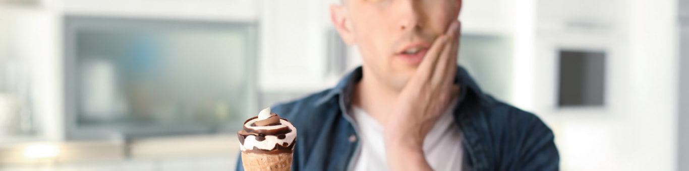 Caucasian man wincing in pain while eating ice cream.