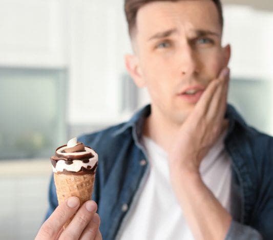 Caucasian man wincing in pain while eating ice cream.