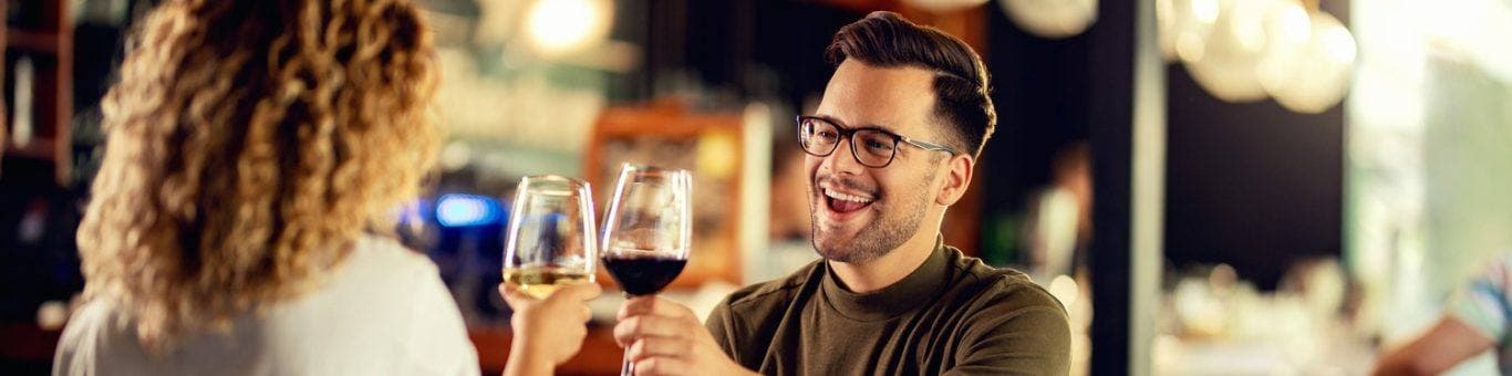 Man and woman toasting wine glasses while having dinner at a restaurant or bar.