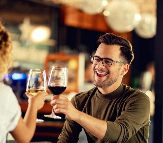 Man and woman toasting wine glasses while having dinner at a restaurant or bar.