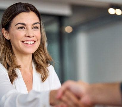 Smiling woman in white button-down shirt shaking hands with person in front.