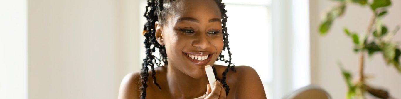 Woman with curly ponytail and orange towel putting lip balm in front of mirror.