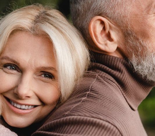 Blonde woman smiling while hugging man in brown turtleneck.