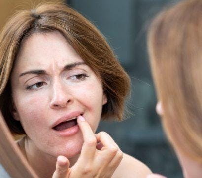 A woman checks her upper teeth in front of a mirror
