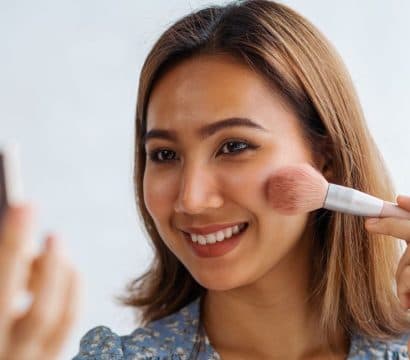 Smiling woman applying blush with a brush.