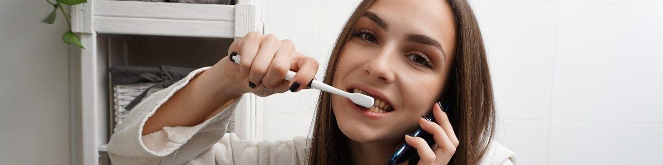 Brunette woman brushing teeth while talking on phone.