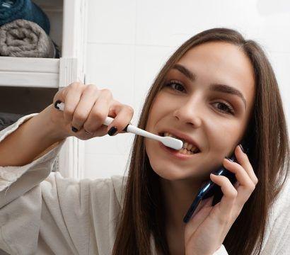 Brunette woman brushing teeth while talking on phone.