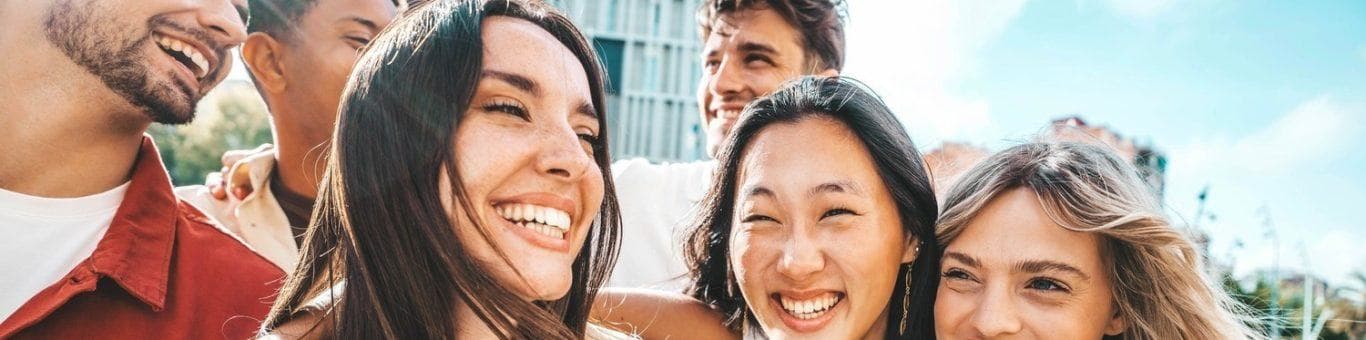 Multiethnic group of friends with three men and three women smiling while walking on a city street.