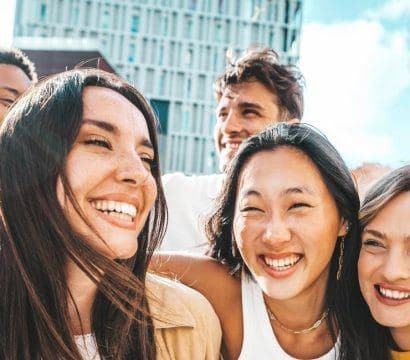 Multiethnic group of friends with three men and three women smiling while walking on a city street.