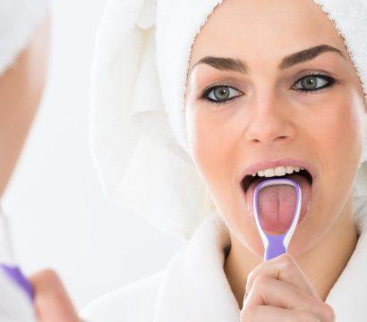 Woman in robe using a tongue scraper.