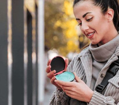 Brunette in ponytail holding a blue aligner case outdoors.