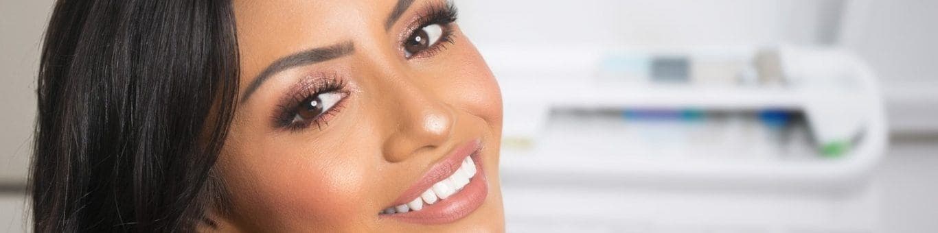 Woman in a dentist’s office smiling happily and showing off white, bonded teeth.