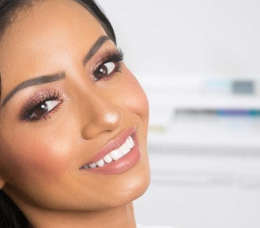 Woman in a dentist’s office smiling happily and showing off white, bonded teeth.