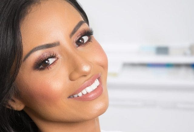 Woman in a dentist’s office smiling happily and showing off white, bonded teeth.