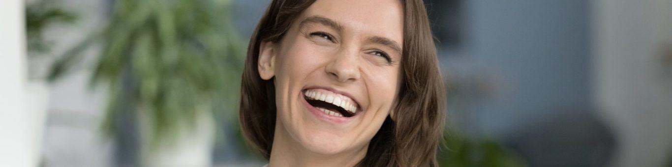 Happy young brunette woman in a white shirt smiling with gums exposed.