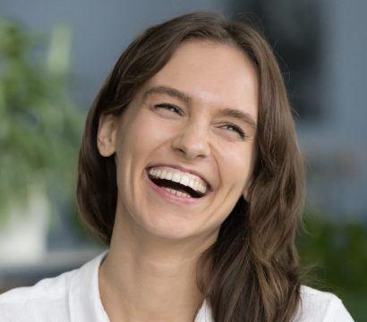 Happy young brunette woman in a white shirt smiling with gums exposed.