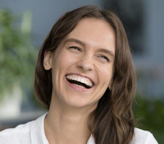 Happy young brunette woman in a white shirt smiling with gums exposed.