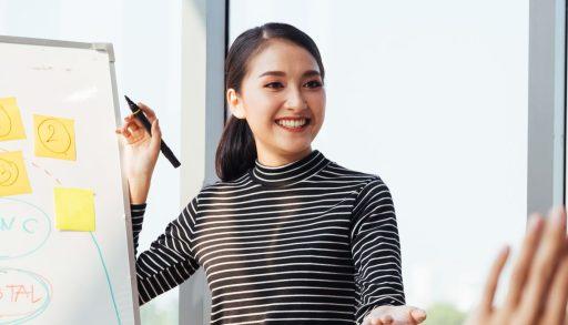 Asian woman smiling while giving presentation to male colleagues.