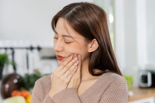 Asian woman holding cheek as if in pain.