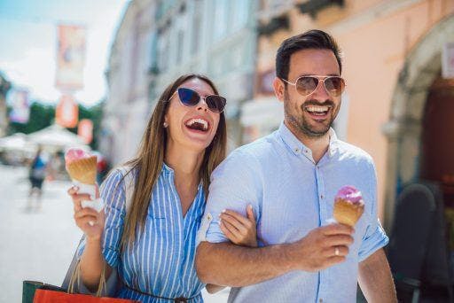 Couple laughing and eating ice cream outdoors. 