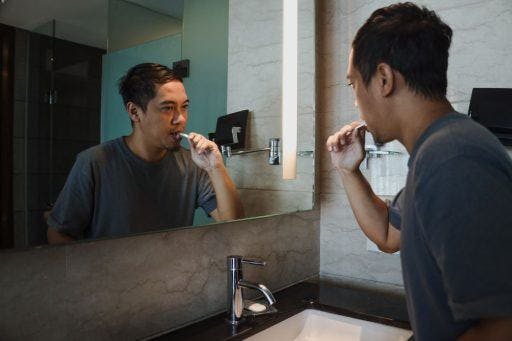 Man brushing his teeth in front of a mirror.