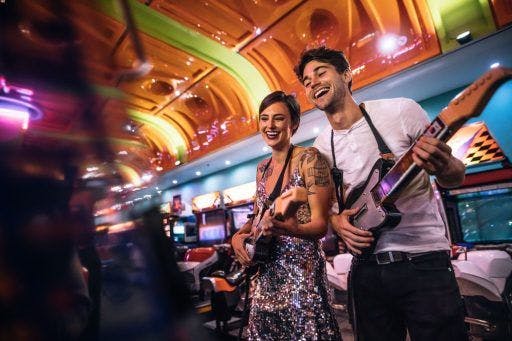 A man and woman playing with electronic guitars at the arcade.