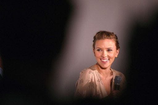 Scarlett Johansson in beige smiling in the spotlight.